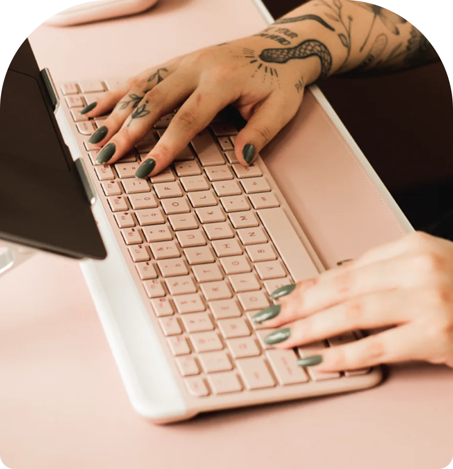Mãos tatuadas digitando em um teclado rosa